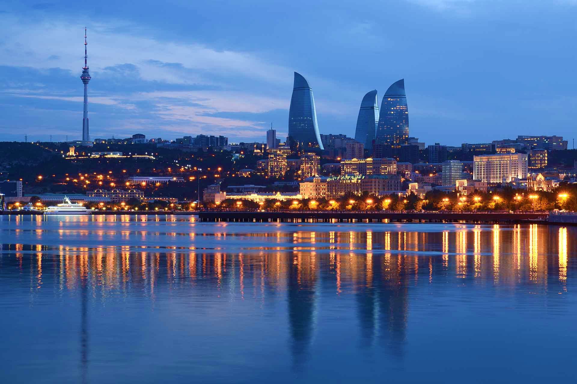 Baku city skyline at dusk with illuminated Flame Towers and TV tower reflected in the Caspian Sea